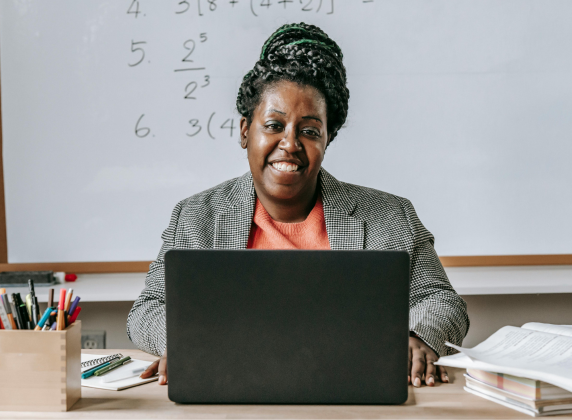 A Black female educator at her desk in front of a laptop, smiling at the camera