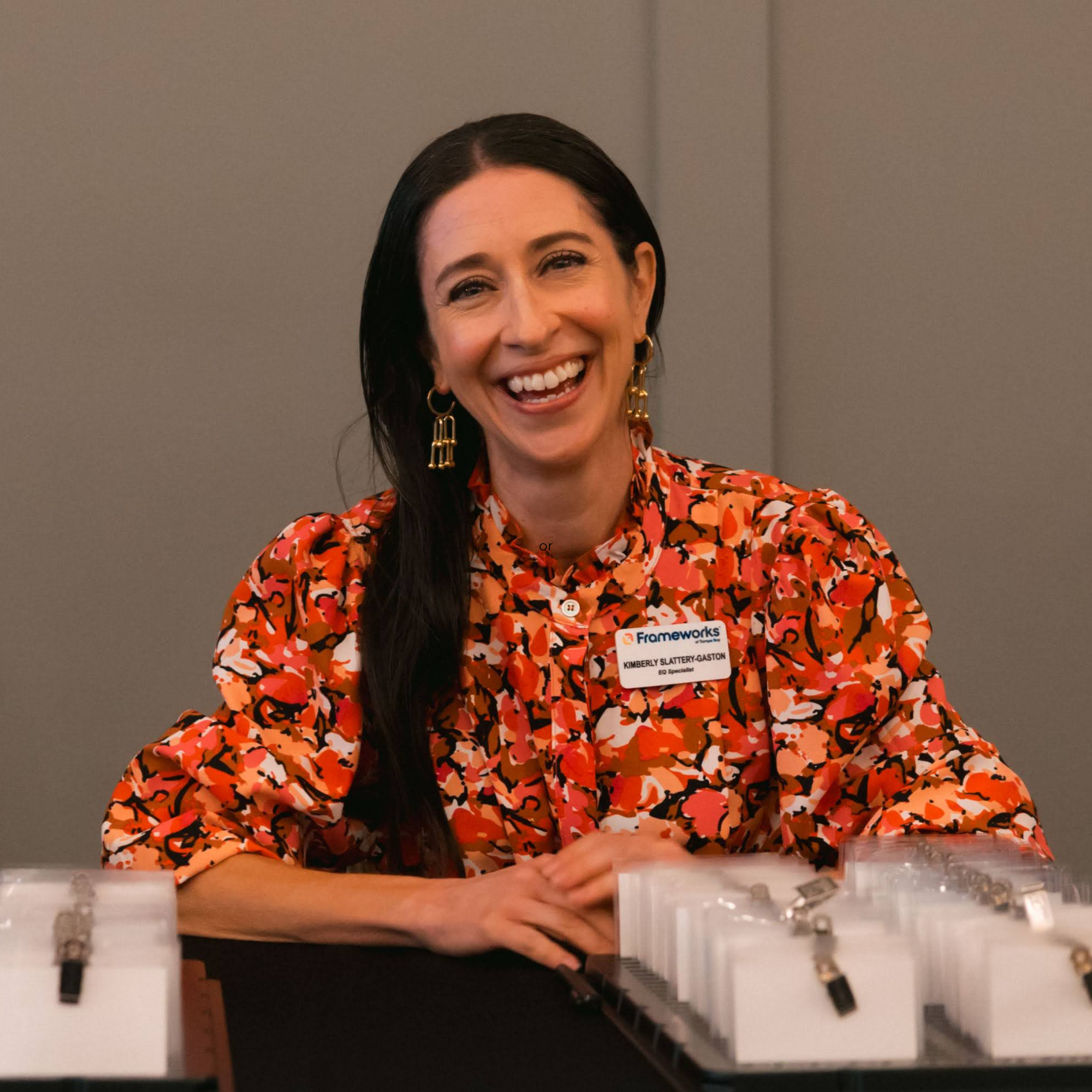 Frameworks team member Kimberly, a white woman with long brown hair smiles into the camera wearing a orange floral top