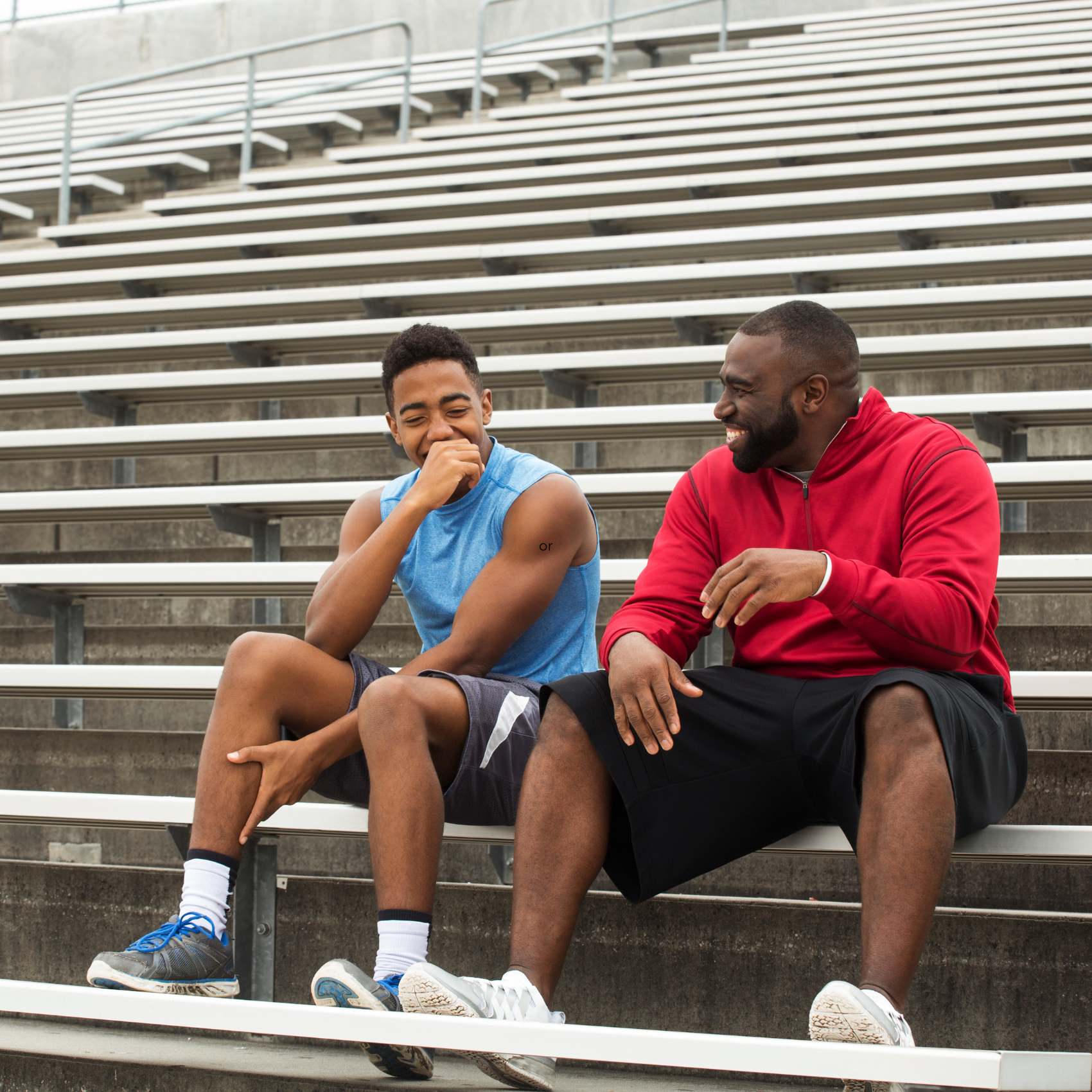 A Black male adult in a red sweatshirt mentoring a Black teen boy who is smiling