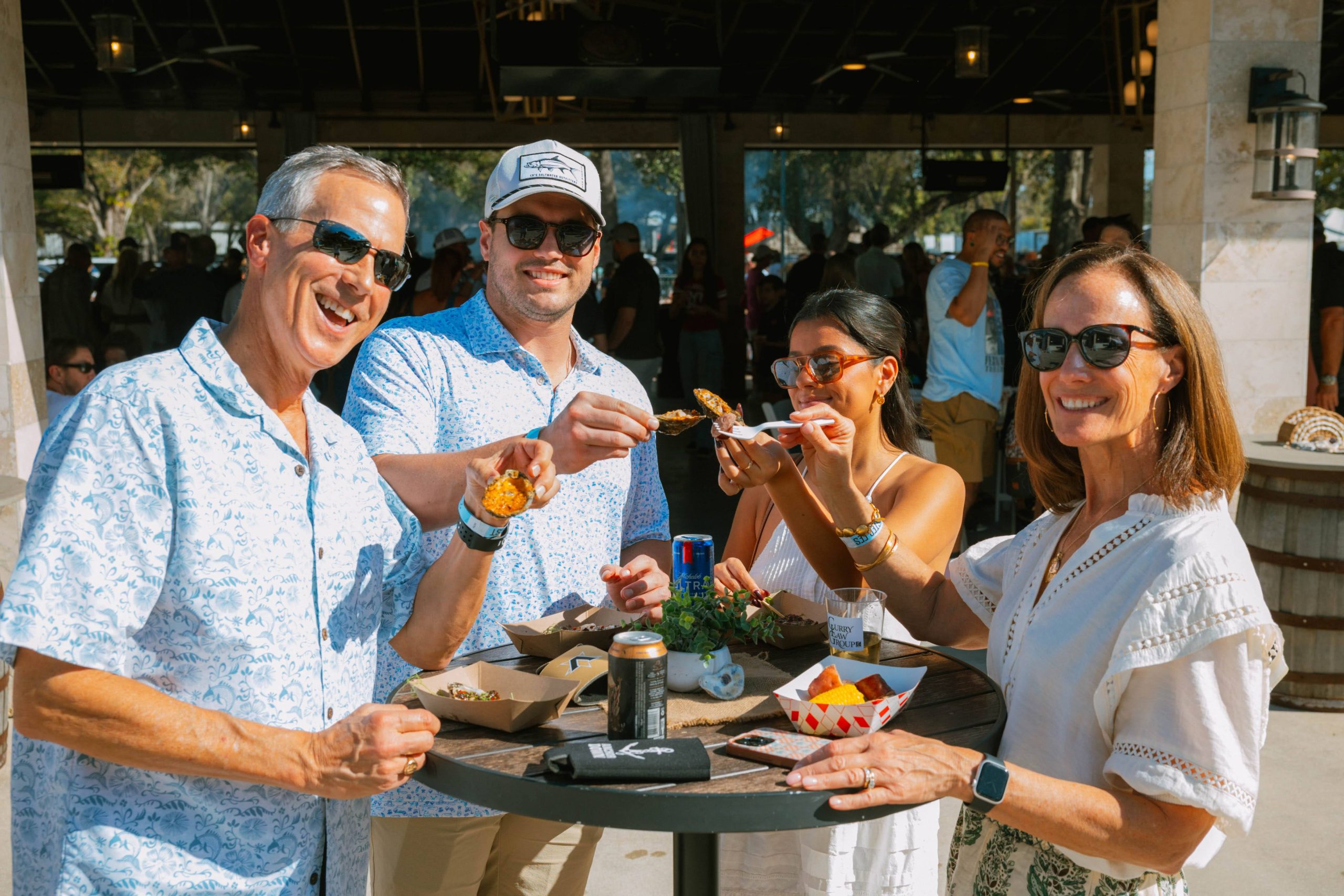 Four people, two men and two women, hold oysters in the air at Frameworks of Tampa Bay's Tampa Oyster Fest